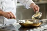 Professional chef spreading margarine on a stainless steel pan, demonstrating expert cooking techniques