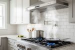 Stainless steel range hood mounted above gas cooktop actively removing cooking smoke and steam from kitchen air
