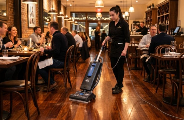 A soft brush vacuum cleaning a polished hardwood restaurant floor between dining tables